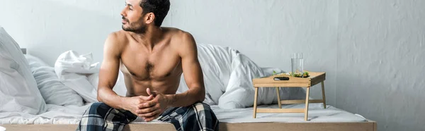 Panoramic shot of handsome bi-racial man sitting on bed in morning — Stock Photo