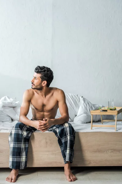 Красивый двурасовый мужчина сидит на кровати и смотрит в сторону утром — стоковое фото