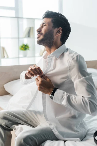 Handsome bi-racial man dressing up and sitting on bed in morning — Stock Photo