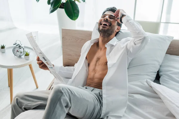 Guapo y sonriente bi-racial hombre sosteniendo periódico en la mañana - foto de stock