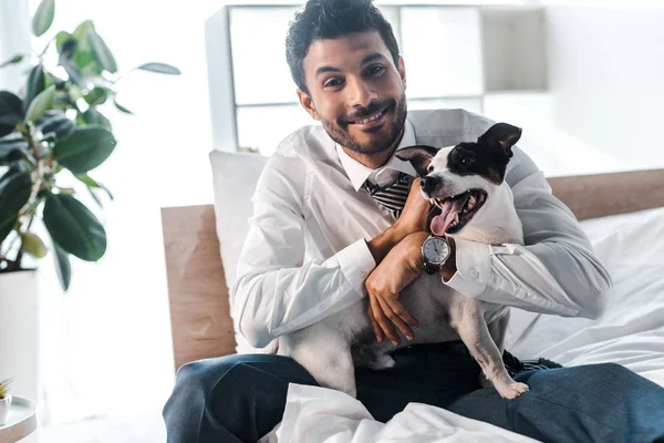 Sonriente hombre de negocios bi-racial acariciando Jack Russell Terrier en la mañana en casa - foto de stock