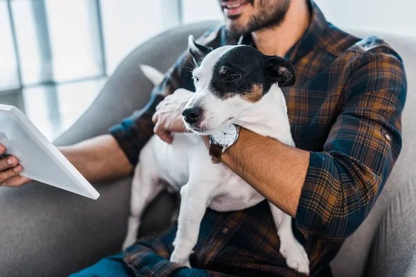 Corte vista de sorrir bi-racial homem segurando Jack Russell Terrier e tablet digital — Fotografia de Stock