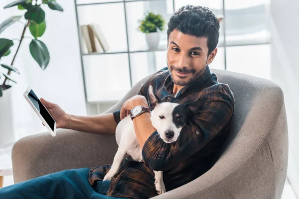 Smiling and handsome bi-racial man holding Jack Russell Terrier and digital tablet — Stock Photo