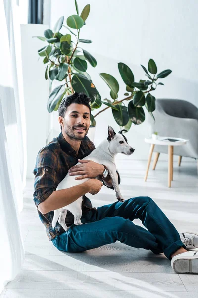 Homme bi-racial souriant et beau tenant Jack Russell Terrier — Photo de stock