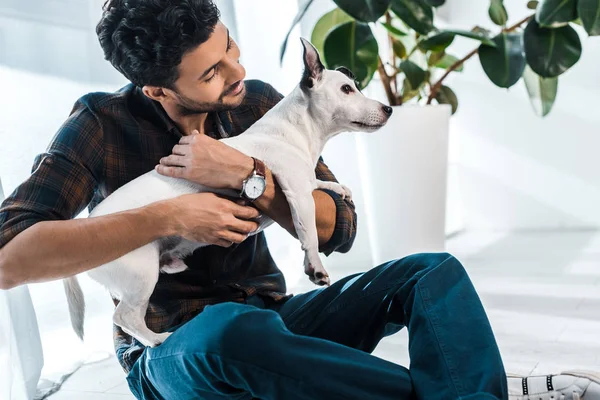 Homme bi-racial souriant et beau tenant Jack Russell Terrier — Photo de stock