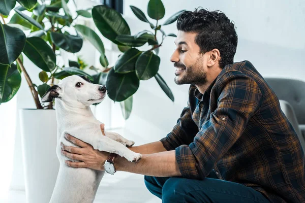 Vista lateral de bonito e sorridente bi-racial homem segurando jack russell terrier — Fotografia de Stock