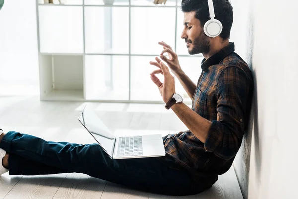 Side view of handsome and smiling bi-racial man with laptop listening music — Stock Photo