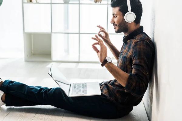 Vista lateral de hombre bi-racial guapo y sonriente con portátil escuchar música - foto de stock