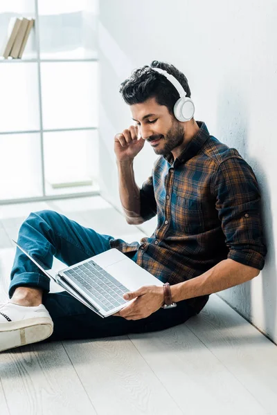 Schöner und lächelnder Mann mit Laptop, der Musik hört — Stockfoto