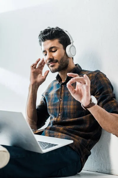 Vista de ángulo bajo de hombre bi-racial guapo y sonriente con portátil escuchar música - foto de stock