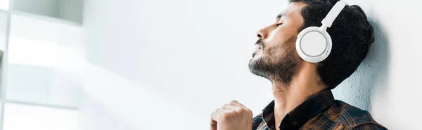 Panoramic shot of handsome bi-racial man with closed eyes listening music — Stock Photo