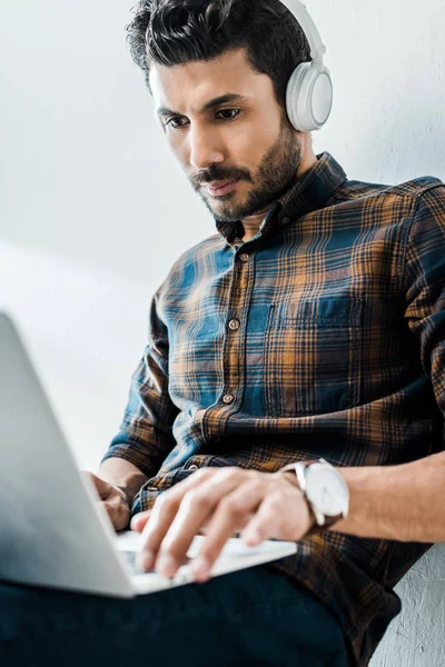 Selektiver Fokus eines gutaussehenden, birassischen Mannes, der Laptop benutzt und Musik hört — Stockfoto