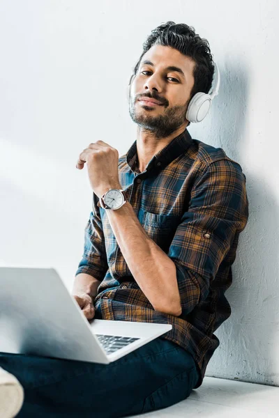 Handsome and smiling bi-racial man with laptop listening music — Stock Photo