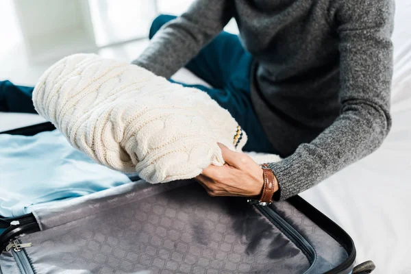 Обрізаний вид на бі-расового чоловіка в светрі, упаковка дорожньої сумки в квартирі — стокове фото