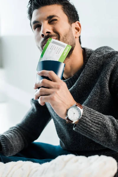 Handsome and pensive bi-racial man in sweater holding passport with air ticket — Stock Photo