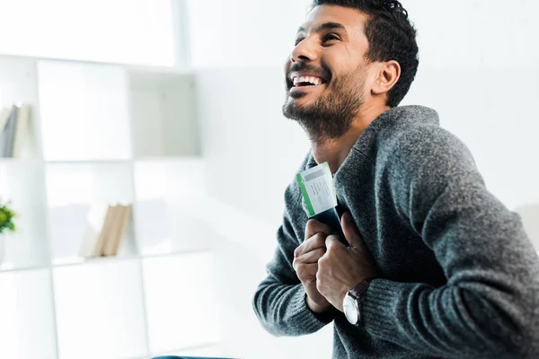 Bonito e sorridente bi-racial homem em suéter segurando passaporte com bilhete de ar — Fotografia de Stock