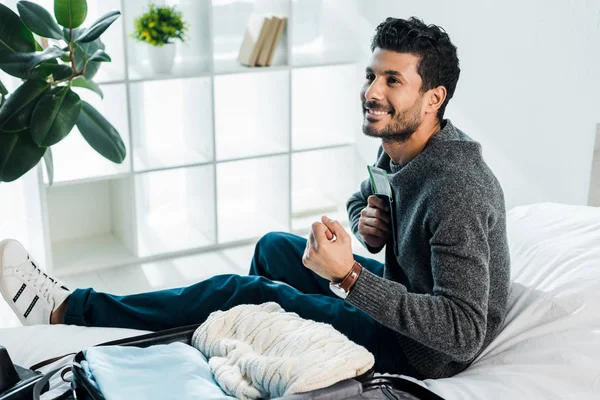 Handsome and smiling bi-racial man in sweater holding passport with air ticket and showing yes gesture — Stock Photo