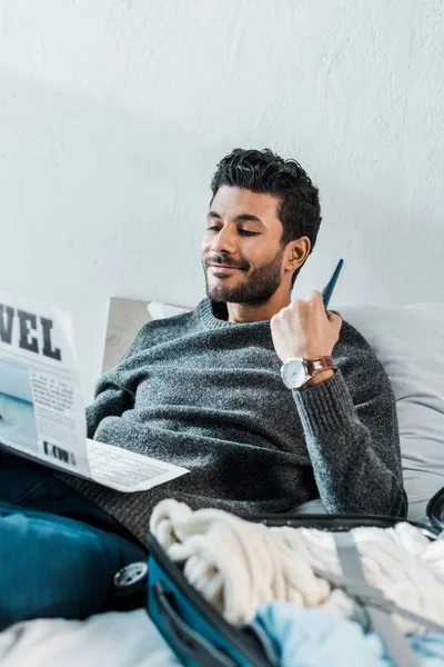 Guapo y sonriente bi-racial hombre en suéter leyendo periódico - foto de stock