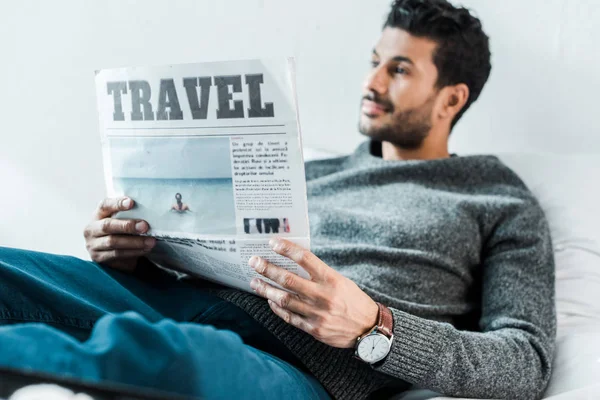 Selektiver Fokus eines gutaussehenden und lächelnden birassischen Mannes, der eine Zeitung mit Schriftzug Reise in der Hand hält — Stockfoto