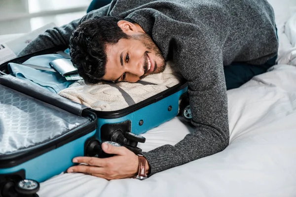 Bello e sorridente uomo bi-razziale sdraiato sulla borsa da viaggio — Foto stock
