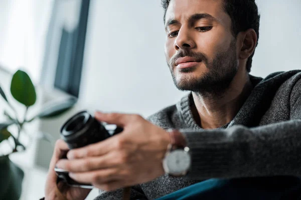 Vista de ángulo bajo del hombre bi-racial guapo que sostiene la cámara digital - foto de stock