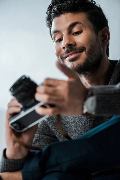 Baixo ângulo vista de bonito e sorridente bi-racial homem segurando câmera digital — Fotografia de Stock