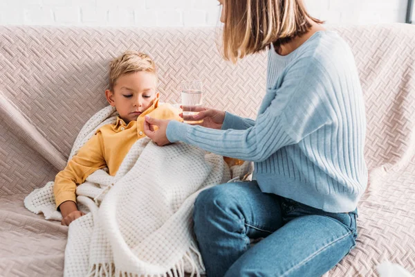 Mãe dando remédio para filho doente envolto em cobertor — Fotografia de Stock