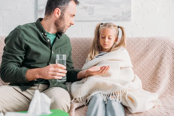 Padre attento che tiene un bicchiere d'acqua e dà pillole alla figlia triste e malata — Foto stock