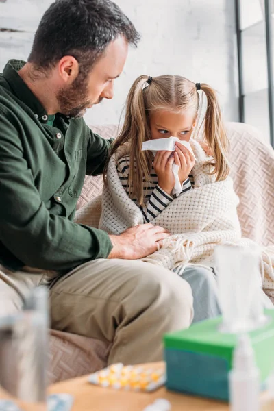 Selective focus of man sitting near sick daughter sneezing in napkin — Stock Photo