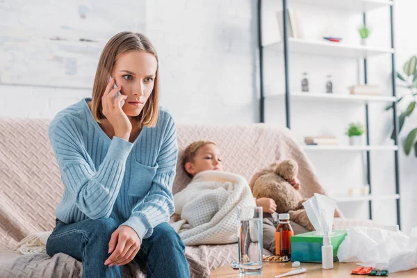 Madre preocupada hablando en el teléfono inteligente mientras está sentado cerca de hijo enfermo - foto de stock