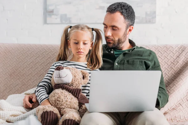 Upset, sick child using laptop with father while sitting on sofa — Stock Photo
