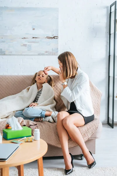 Woman in formal wear talking on smartphone and touching forehead of sick daughter — Stock Photo