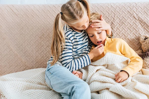 Attentive sister giving pill to diseased brother and touching his forehead — Stock Photo