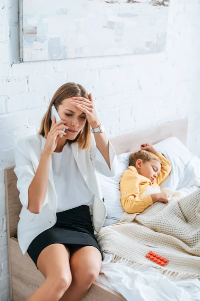 Donna sconvolto parlando su smartphone mentre seduto vicino figlio malato — Foto stock