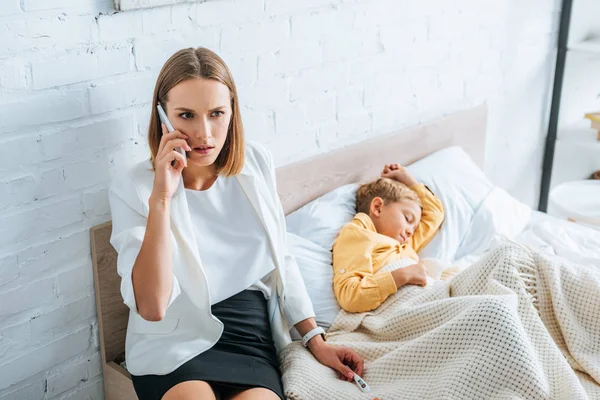Worried woman talking on smartphone while sitting near diseased son — Stock Photo