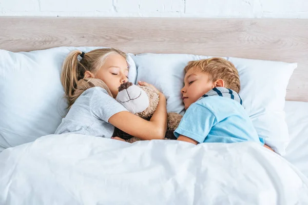 Bruder und Schwester schlafen mit Teddybär im Bett — Stockfoto