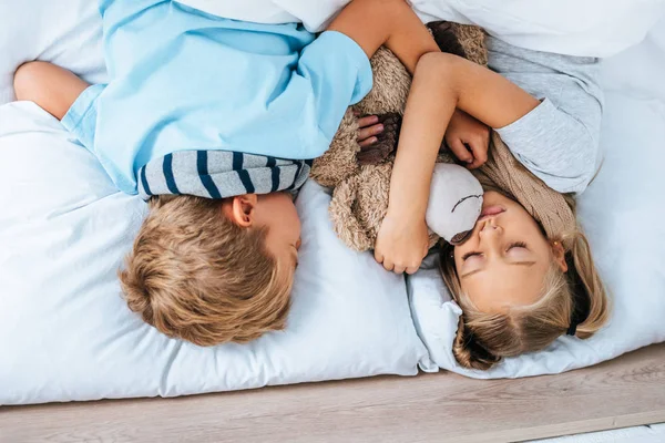 Overhead view of diseased brother and sister sleeping in bed with teddy bear — Stock Photo