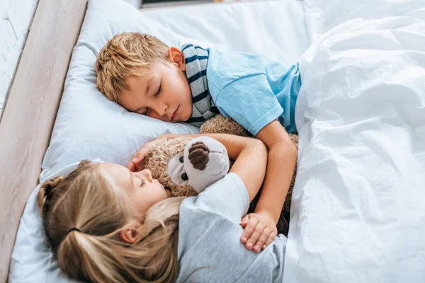 Hermano enfermo y hermana durmiendo en la cama con osito de peluche - foto de stock
