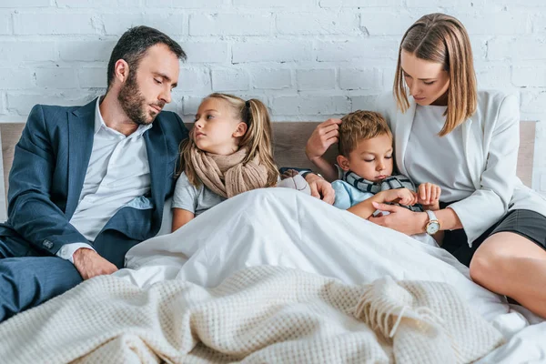 Man and woman in formal wear lying in bed near sick children — Stock Photo