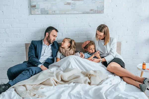 Man and woman in formal wear lying in bed near diseased children — Stock Photo