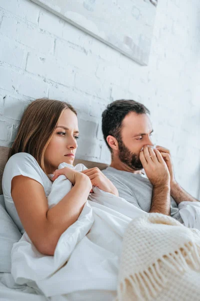 Diseased man sneezing in napkin while lying in bed near sick wife — Stock Photo