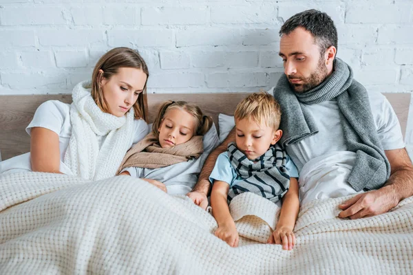 Famille malade dans des foulards chauds couchés dans le lit sous des couvertures — Photo de stock