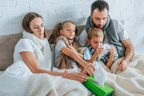 Familia enferma tomando servilletas mientras están acostados en la cama juntos - foto de stock