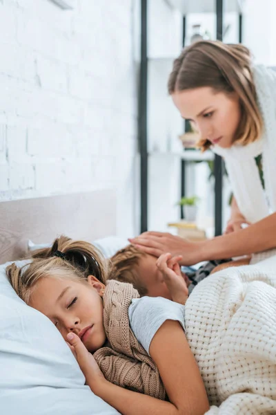 Sorgenvolle Mutter berührt Kopf ihres kranken Sohnes, der in der Nähe der kranken Schwester liegt — Stockfoto