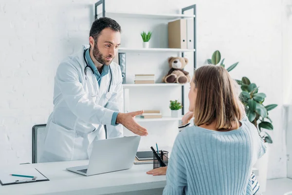 Sorridente médico estendendo a mão para a mulher sentada na mesa — Fotografia de Stock