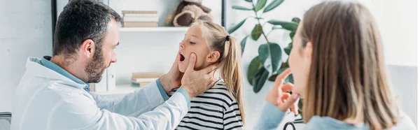 Médecin attentif examinant la gorge de l'enfant près de la mère — Photo de stock