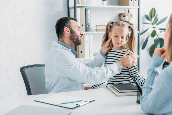 Уважний педіатр, який вивчає дитину біля матері, сидить за столом — Stock Photo