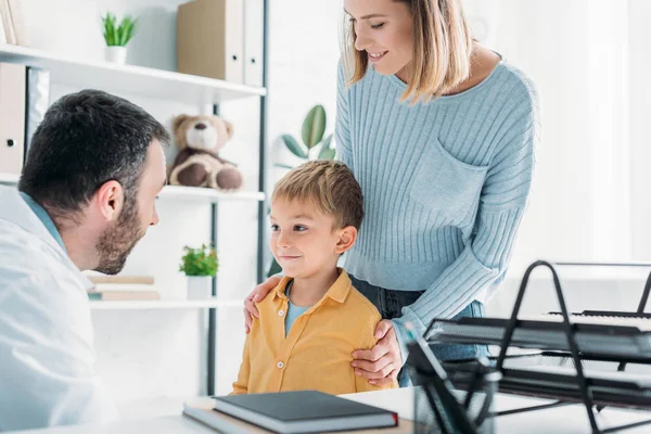 Smiling mother and son standing near attentive pediatrist in hospital — Stock Photo