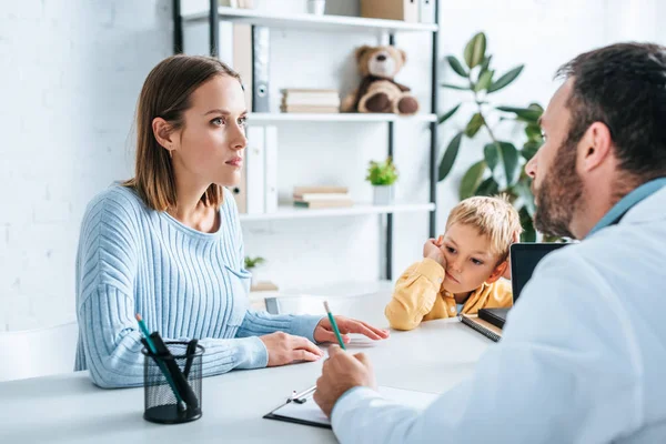 Femme sérieuse avec son fils regardant le médecin à l'hôpital — Photo de stock