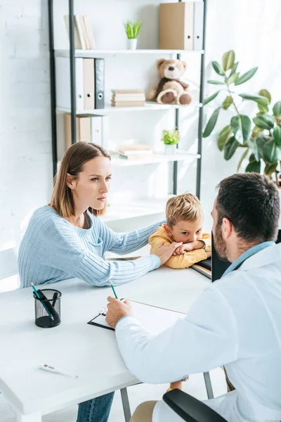 Atenta madre con hijo mirando al médico en el hospital - foto de stock